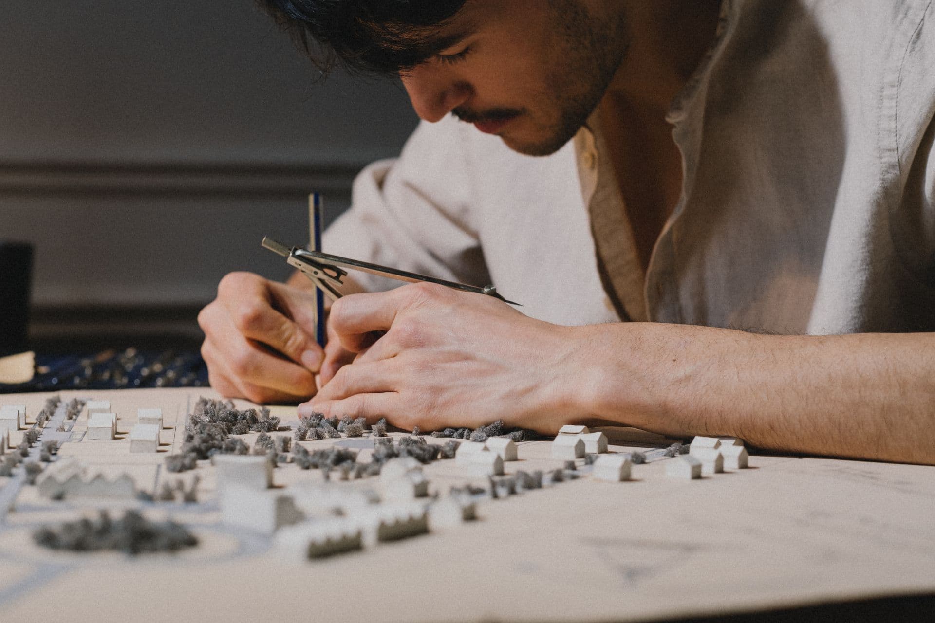 Architect's hands working on a detailed physical massing model with a drafting compass